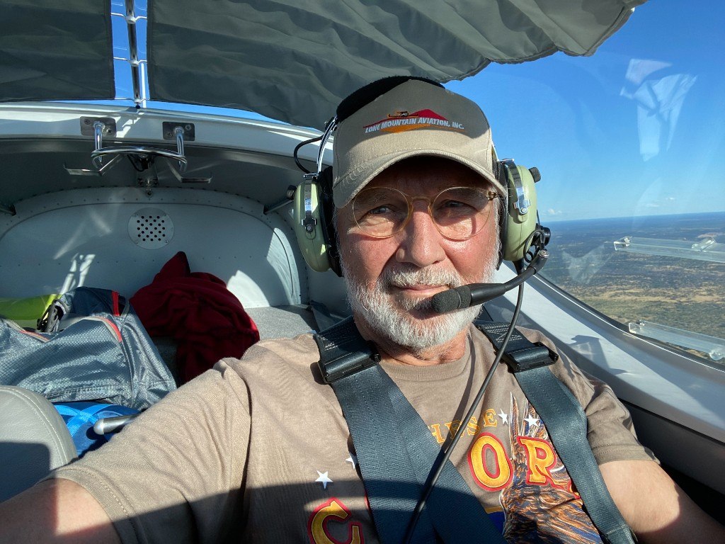 Barry Rickert at the controls of a small aircraft, wearing a headset and smiling
